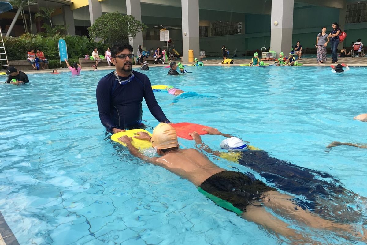 Coach U.K. Singh guiding a child through a front float during a swimming lesson in Singapore