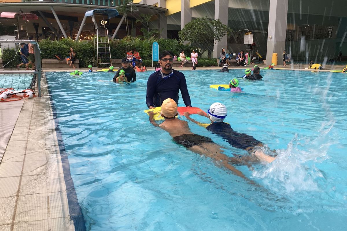 Children practising swimming with kickboards under a coach's close supervision